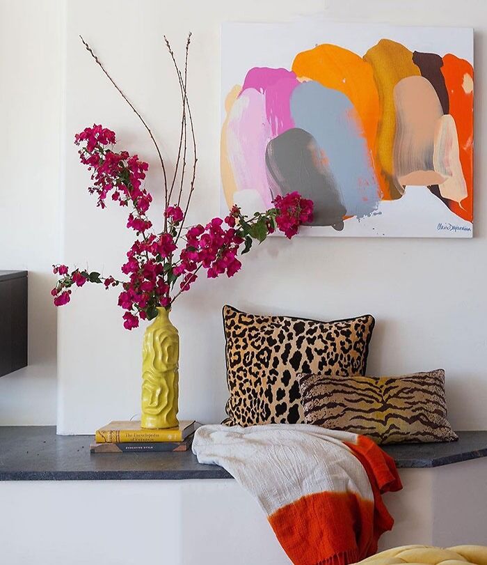 Abstract art above a bed with vibrant pink flowers in a yellow vase, animal print pillows, and cozy textiles for bedroom wall decor ideas.