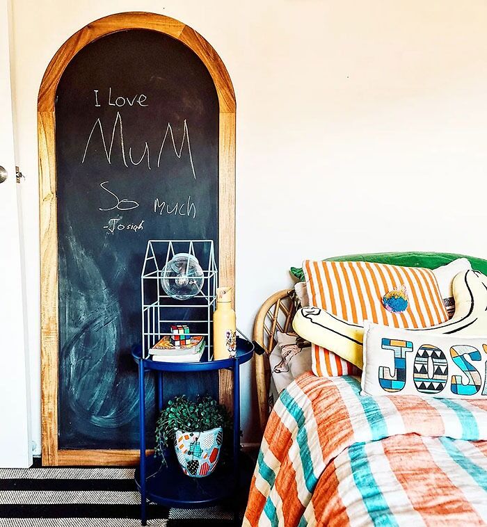Chalkboard bedroom wall decor with wooden frame, cozy bed with colorful striped bedding and decorative pillows.