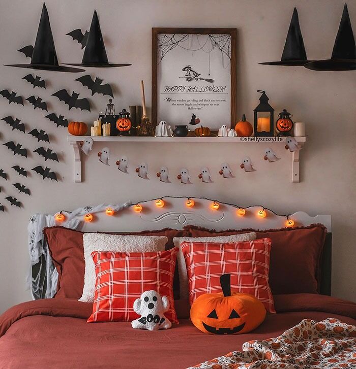 Halloween bedroom wall decor featuring pumpkin lights, ghost garlands, and spooky themed accents on a cozy bed setup.