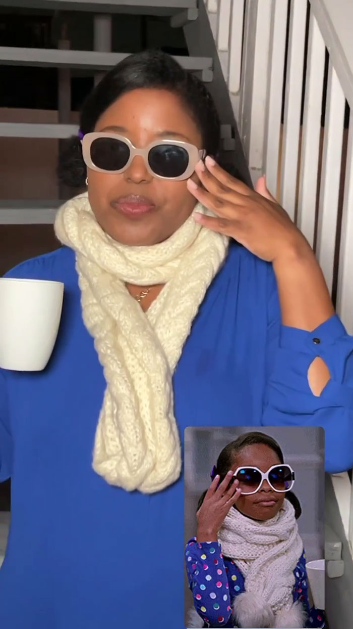Woman dressed in meme-themed outfit with scarf and sunglasses, holding a mug, perfectly embodying the meme concept.