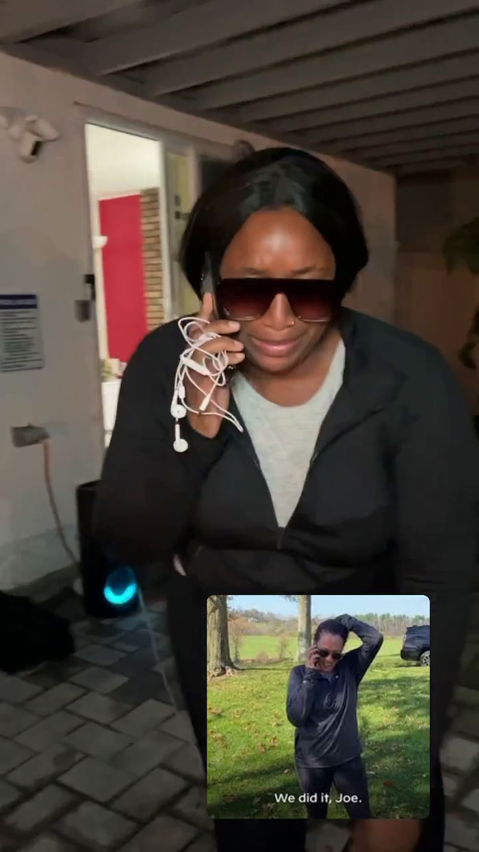 Woman at meme-themed party wearing sunglasses, holding a phone with earbuds tangled around it.