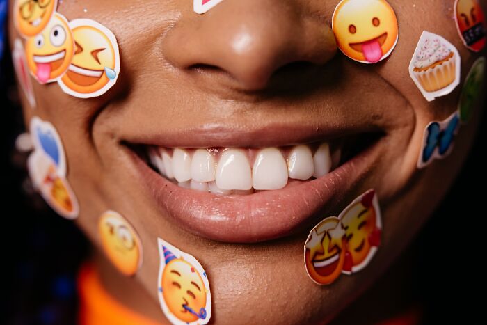 Close-up of a smiling face with various emoji stickers, illustrating unspoken mom code and online conversations.
