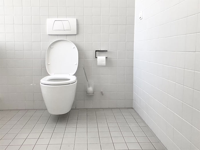 Minimalist white bathroom with a wall-mounted toilet and toilet paper holder illustrating what not to do when visiting the US.