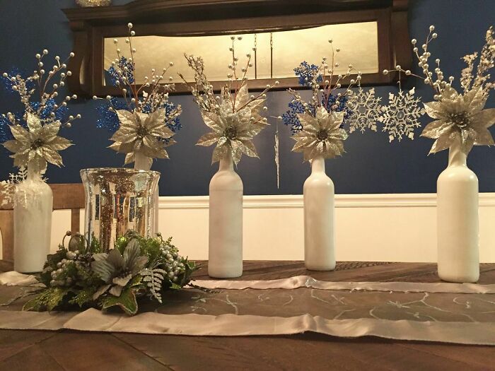 Painted wine bottles with branches and festive decor, showcasing affordable Christmas decor ideas for 2024 celebrations.