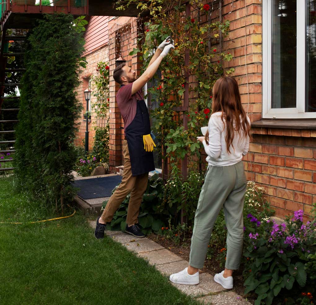 A man working in a garden and a woman standing with a cup