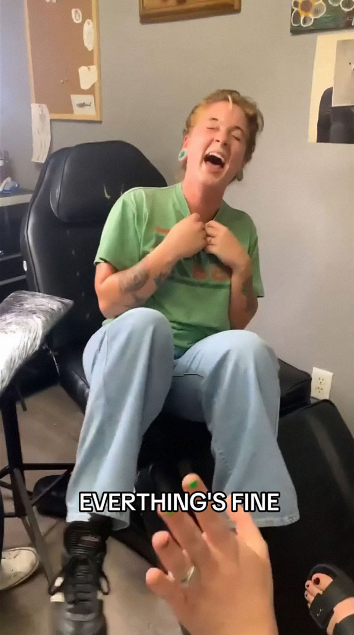 Person in a green shirt laughing on a tattoo chair, experiencing a humorous tattoo blunder, captured for TikTok.
