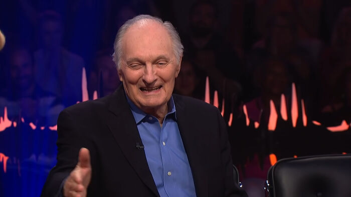 Alan Alda trying to shake someone's hand 