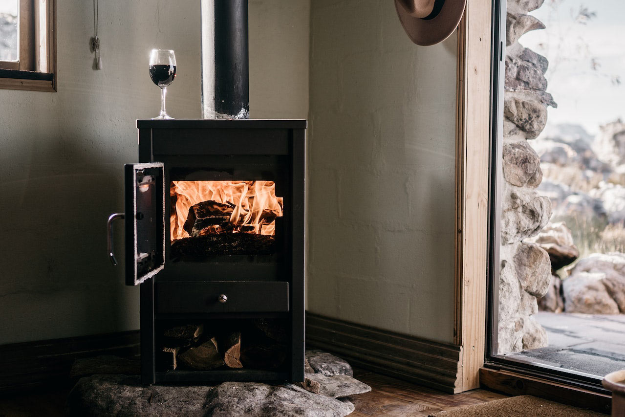 Wood-burning stove on a concrete base with fire inside and a glass of red wine on top of it