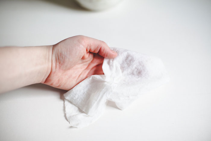 Hand holding a baby wipe, considering its safety for use on dogs.
