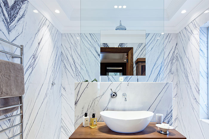 Modern bathroom with white ceramic sink on brown wooden table and elegant marble bathroom tile design on walls.