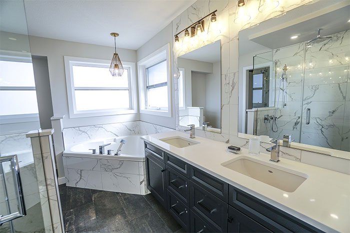 Bathroom featuring white marble tile design on walls, floors, and sinks with modern fixtures and ample natural light.