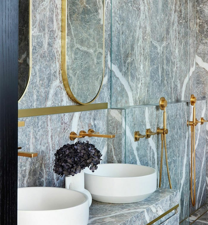 Bathroom with granite tile walls and white sinks featuring gold fixtures for elegant bathroom tile design ideas.