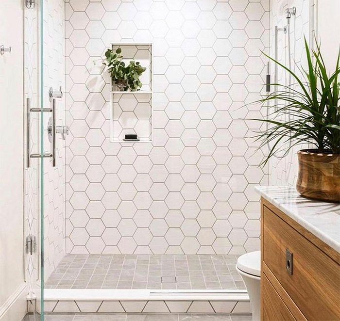 Bathroom with white hexagon tile design on walls and neutral square tile flooring, featuring wooden vanity and green plant.