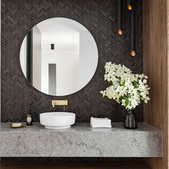 Bathroom with herringbone tile design on wall, round mirror, modern sink, and decorative white flowers on countertop.