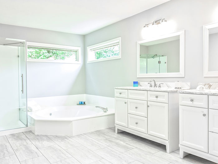 All-white bathroom with ceramic bathtub and white wooden vanity featuring beautiful bathroom tile flooring design.