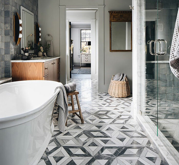 Bathroom with geometric gray and white bathroom tile design ideas on flooring next to bathtub and wooden sink cabinet.