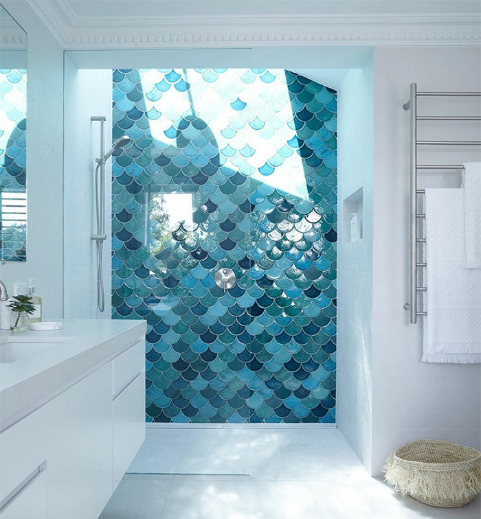 White bathroom featuring blue fish-scale bathroom tile design on the shower wall creating a vibrant accent.