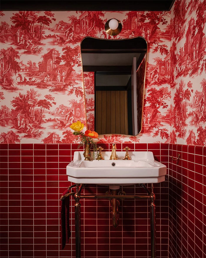 Red bathroom featuring rectangular tile design on walls with floral wallpaper and a white sink with gold fixtures.