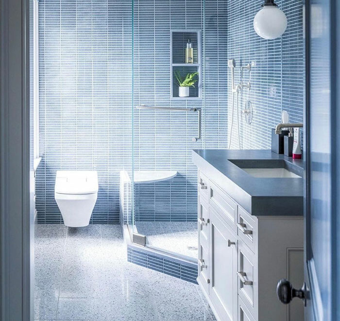 Blue bathroom with small rectangular tile design on walls and flooring, featuring white cabinets and modern fixtures.