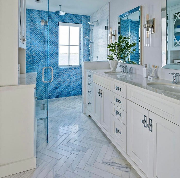 Blue bathroom with mosaic shower tiles, white chevron floor tiles, and white sink showcasing bathroom tile design ideas.