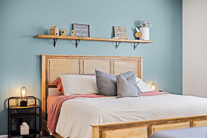 Cozy bedroom interior featuring wooden bed frame and minimalist bedroom wall decor ideas on blue wall background.