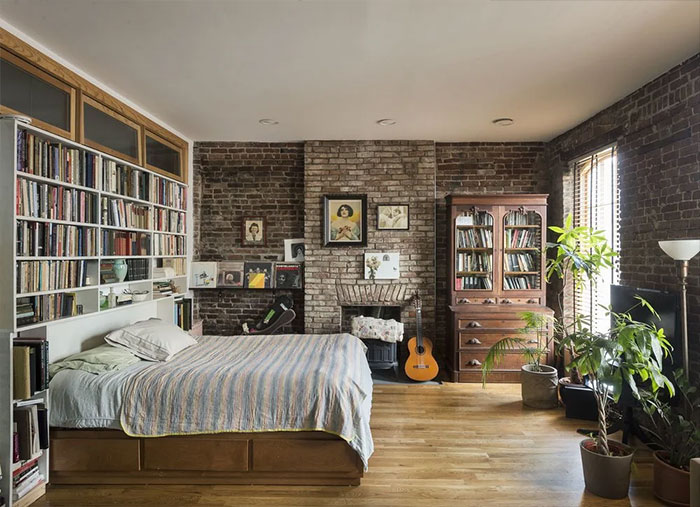 Cozy bedroom interior featuring brick walls, framed art, bookshelves, and natural light for bedroom wall decor ideas.