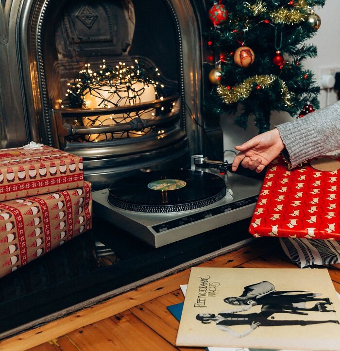 Cozy Christmas decor with affordable wrapped gifts near a fireplace and a record player playing vinyl music.