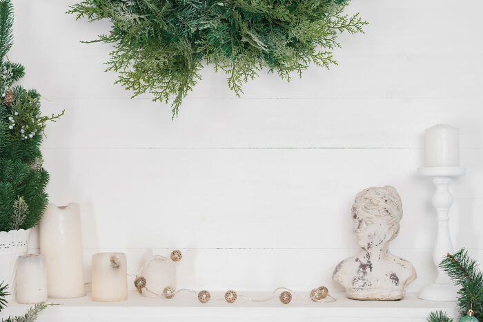 Affordable Christmas decor with candles, greenery, and a rustic statue near a white wall for budget-friendly holiday style.