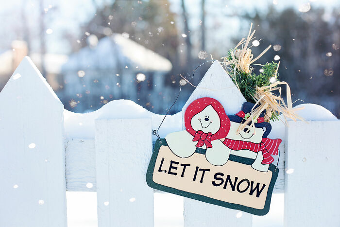 Christmas signboard reading Let It Snow on a white fence, showcasing affordable Christmas decor in snowy outdoor setting.