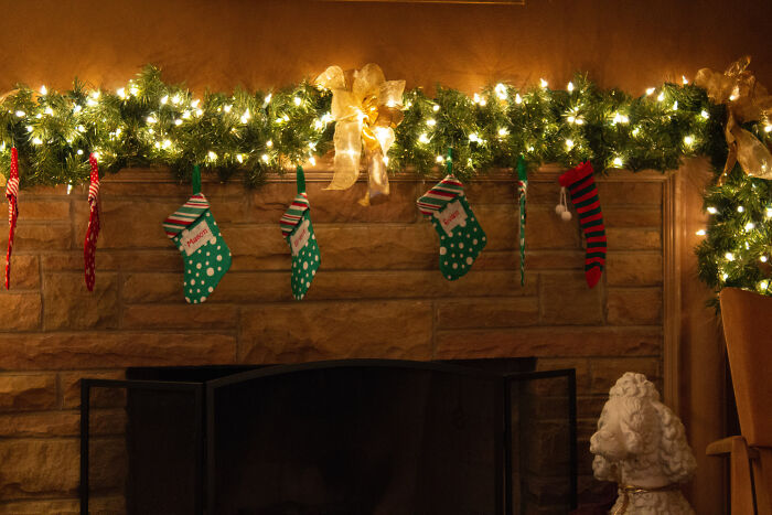 Colorful Christmas stockings hanging by a fireplace with lit garland showcasing affordable Christmas decor ideas.