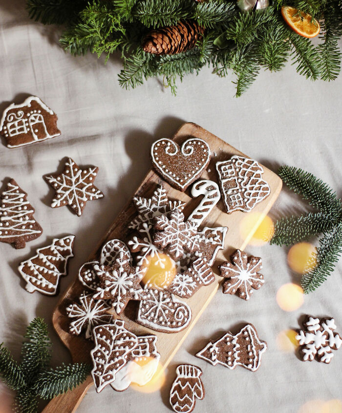 Gingerbread cookies with white icing on a cutting board surrounded by pine branches, showcasing affordable Christmas decor ideas.