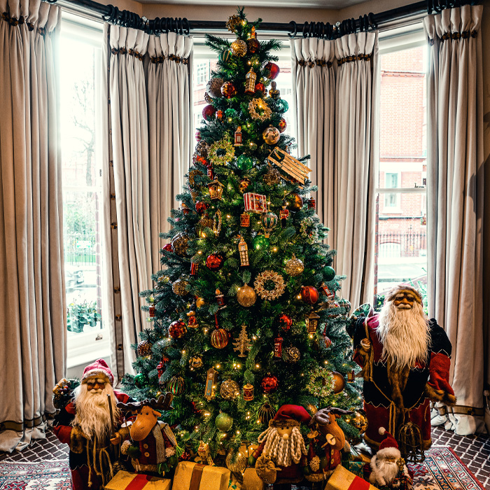 Christmas tree decorated with lights and ornaments surrounded by Santa Claus dolls and festive decorations.
