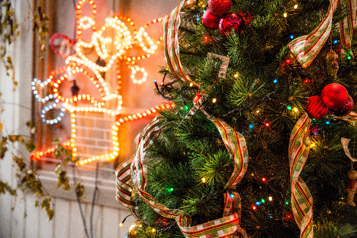 Green and red Christmas tree decorated with ribbons and lights next to a glowing neon holiday sign for festive celebrations.