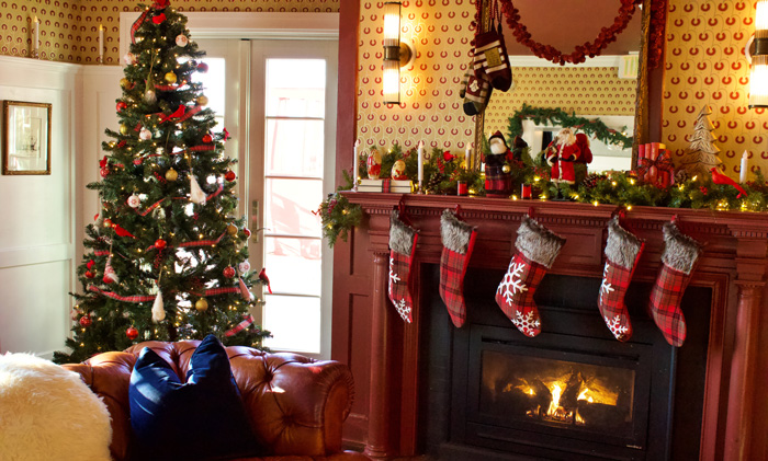 Christmas tree decorations with lights and ornaments beside a cozy fireplace with hanging festive stockings.