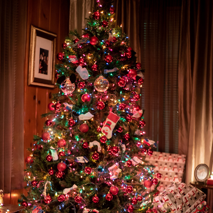 Christmas tree decorated with colorful lights and red baubles, surrounded by wrapped presents for festive celebrations.
