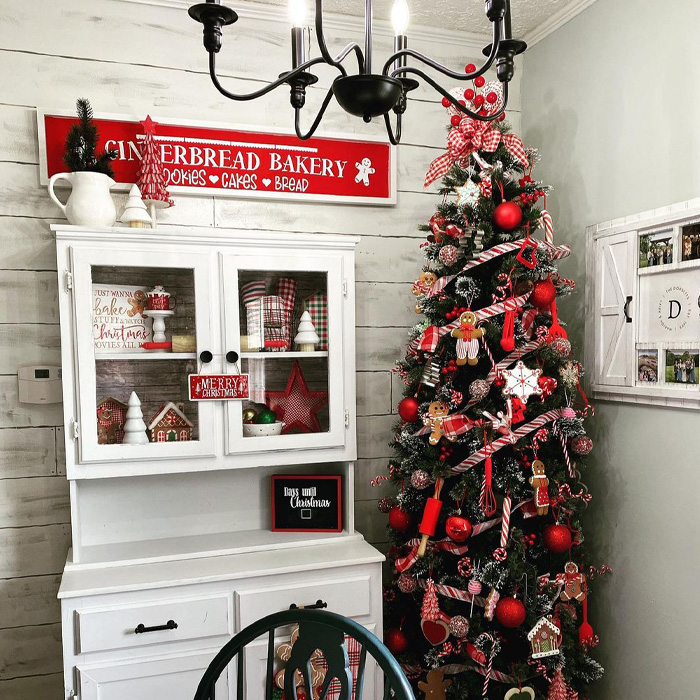 Red Christmas tree decorated with gingerbread and candy canes next to a white china cabinet for magical Christmas tree decorations.