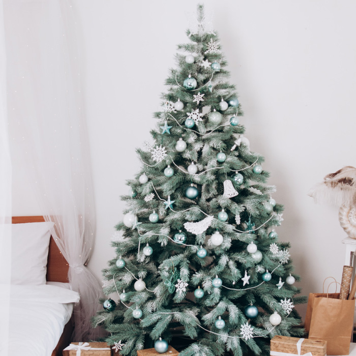 Presents wrapped in brown paper placed under a Christmas tree decorated with blue and white ornaments for festive celebrations
