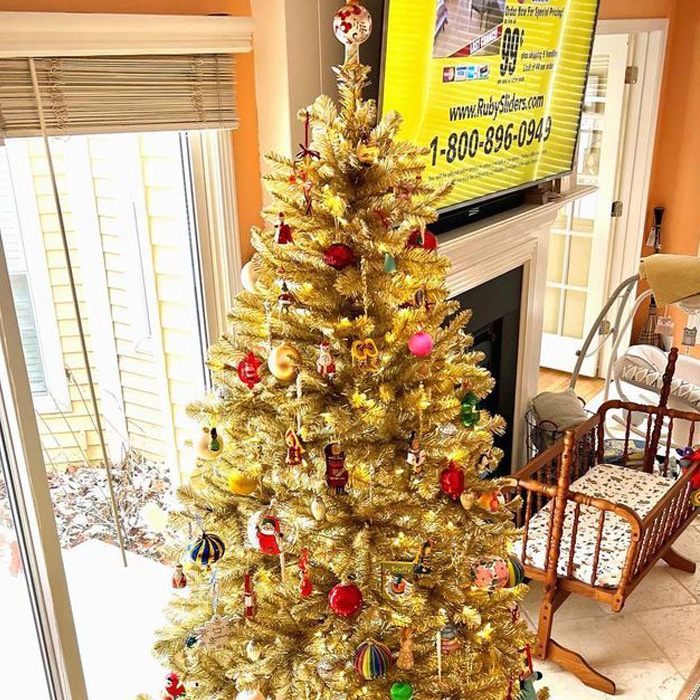 Golden Christmas tree decorated with colorful ornaments standing next to a cozy fireplace for festive celebrations.