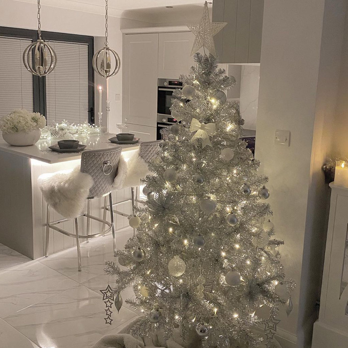 Grey Christmas tree decorated with white and silver ornaments and lights in a modern kitchen setting for Christmas.