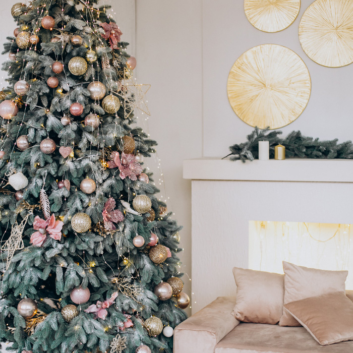Decorated Christmas tree with magical ornaments and wrapped gifts next to a pale pink couch in cozy holiday setting.