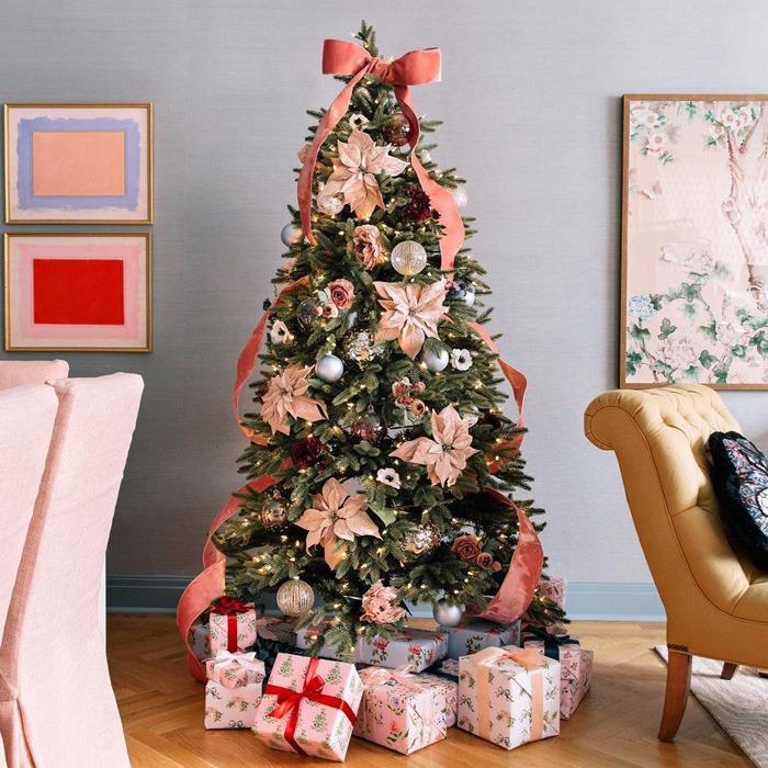 Pale pink Christmas tree decorated with ribbons and flowers, surrounded by wrapped presents for festive celebrations.