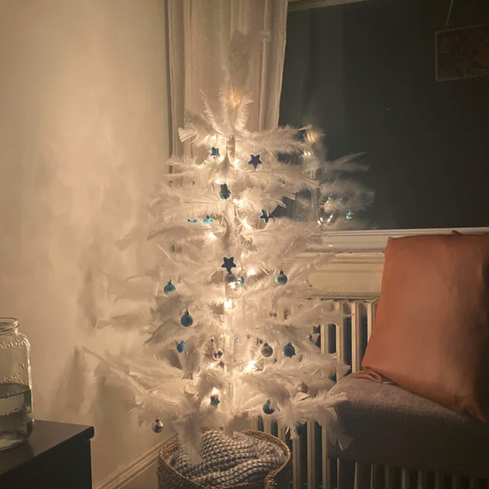 Feathery Christmas tree with blue ornaments and warm lights in a basket, showcasing magical Christmas tree decorations ideas.