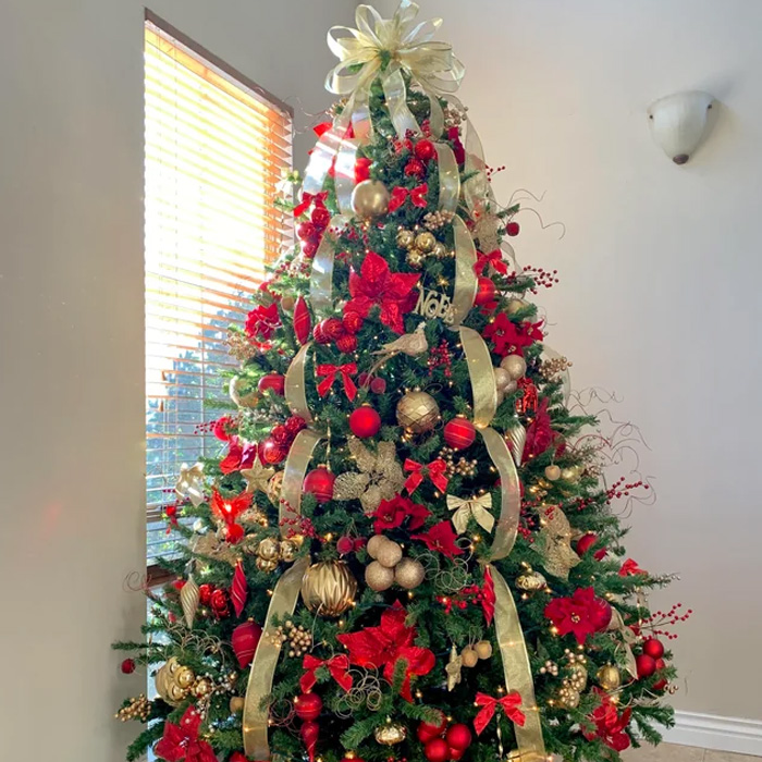 Christmas tree decorated with oversized ribbon topper, red and gold ornaments for magical Christmas tree decorations and ideas.