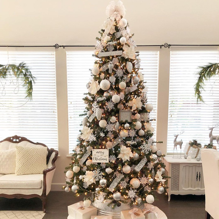 Decorated Christmas tree with white ornaments and lights on a white tree skirt surrounded by wrapped presents for magical celebrations