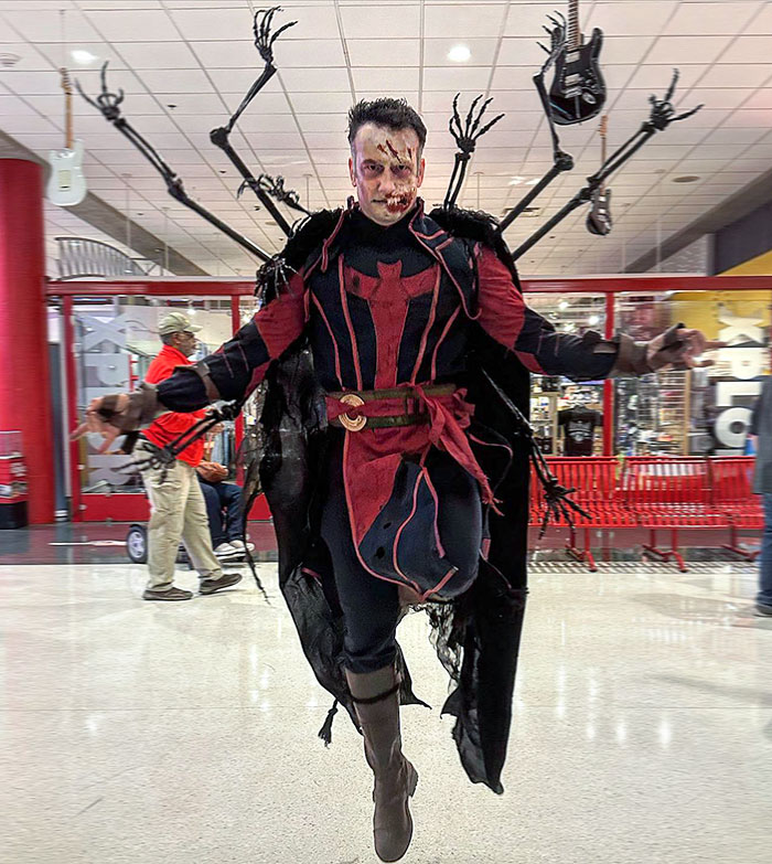 Man wearing a clever Halloween costume with spider legs and face makeup jumping in a public indoor space.