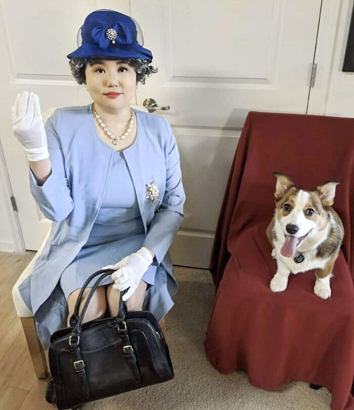 Woman in clever Halloween costume dressed as Queen Elizabeth with a dog sitting next to her on a red-covered chair.