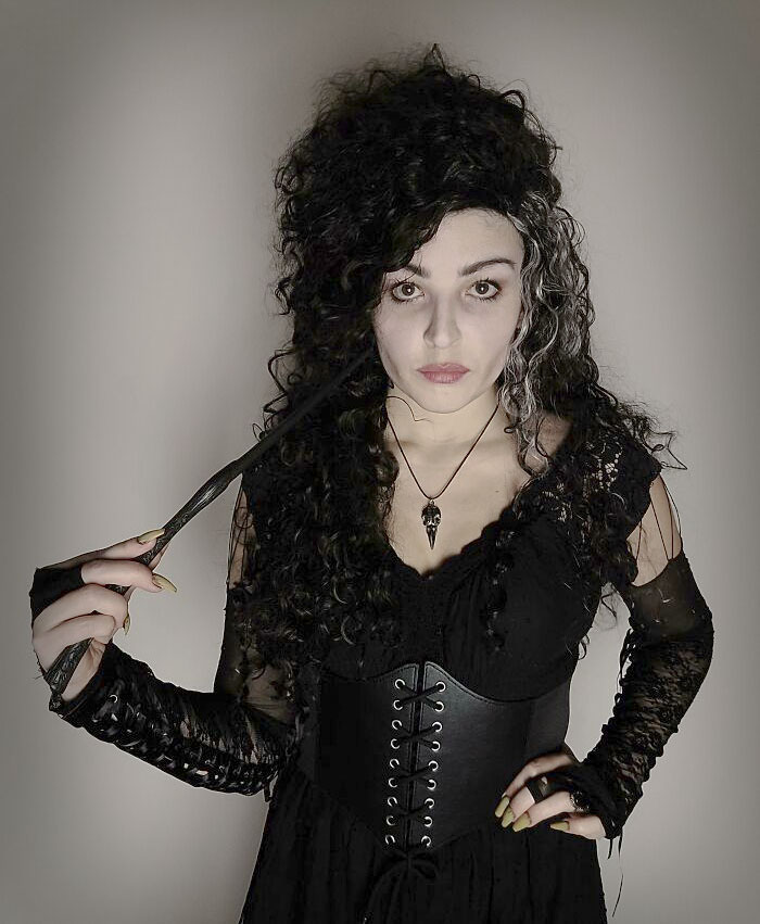 Woman wearing a clever Halloween costume with dark curly hair, black lace dress, and holding a wand for Halloween costumes.