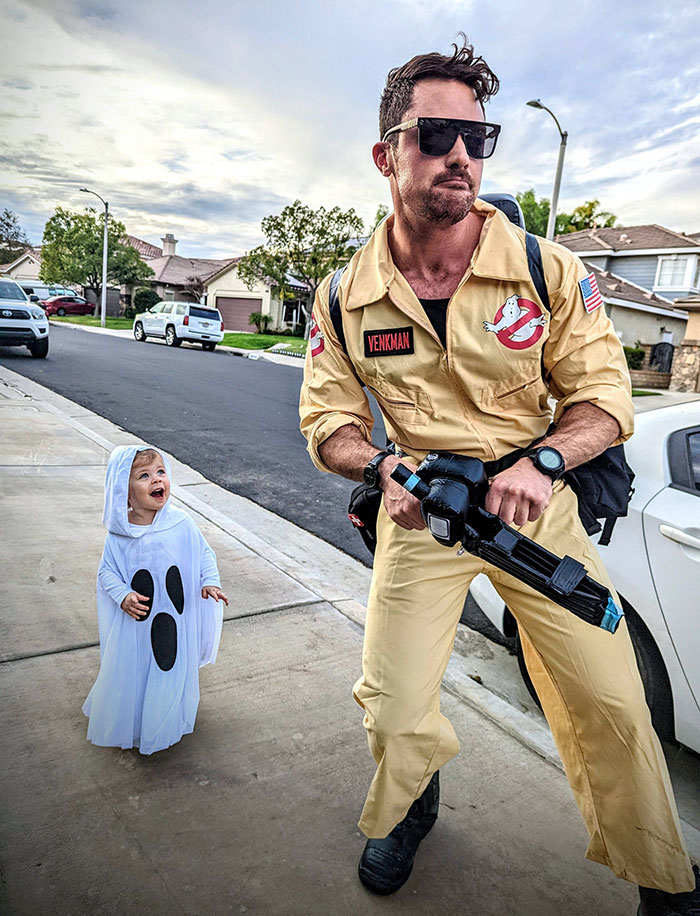 Man dressed as Ghostbuster with child in ghost costume on suburban street for Halloween costumes clever ideas.
