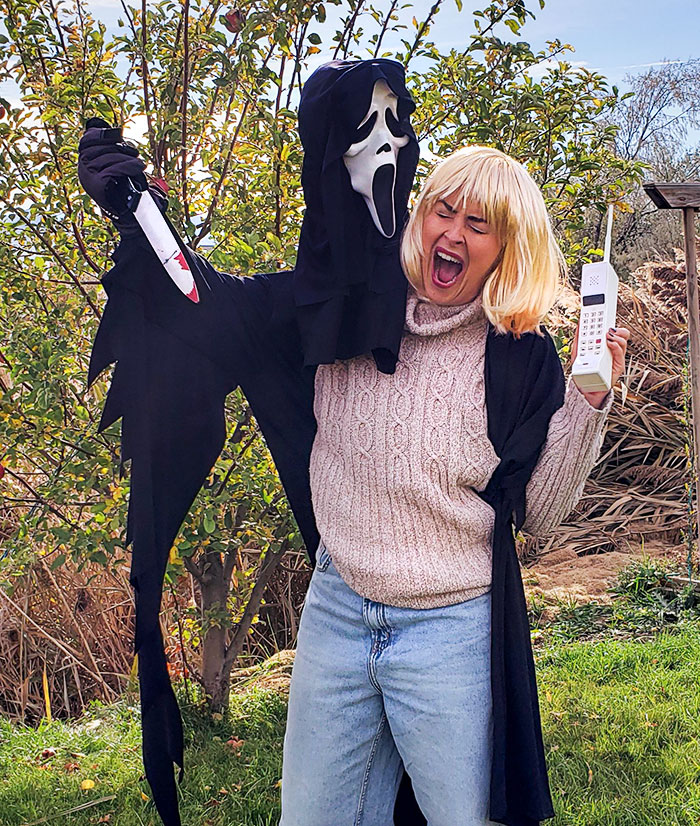 Person dressed in a clever Halloween costume inspired by a classic horror movie character holding a fake knife and phone outdoors.