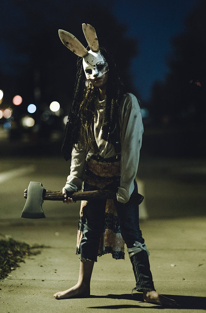 Person wearing a clever Halloween costume with a creepy bunny mask and holding an axe outdoors at night.
